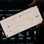 A person holding a cell phone in front of a laptop